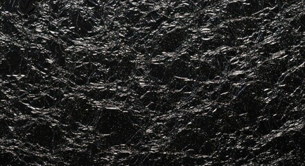 Fototapeta premium Closeup of a dark rugged textured surface with irregular crevices and grain details.