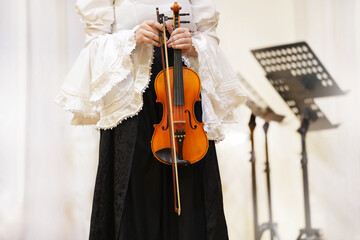 Female musician in elegant attire holds a violin, showcasing her passion for music on stage, with music stands and soft lighting creating a captivating atmosphere