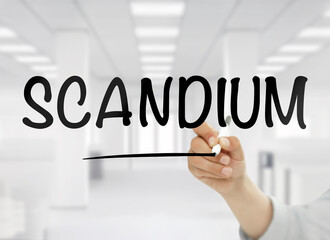 A conceptual image featuring the word scandium handwritten in bold black letters on transparent glass, with a blurred white modern office interior in the background, symbolizing this rare metal&rsquo;s role