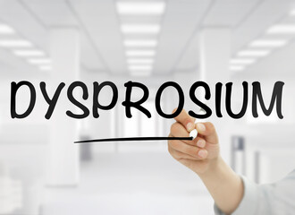 A conceptual image showing the word dysprosium handwritten in bold black letters on transparent glass, with a blurred modern white office interior in the background. This rare earth element theme is s