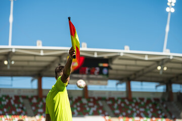 Raised flag by the football sideline referee with ball and the tribune in the background
