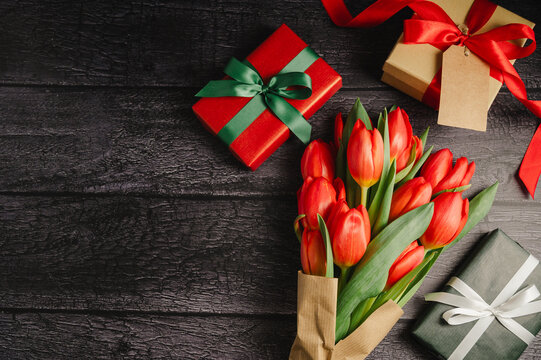 Red tulip bouquet with gift boxes. Easter or birthday holiday black background. - Powered by Adobe