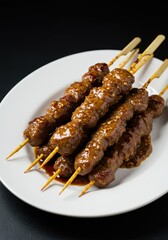 Succulent grilled goat satay skewers served piping hot on a white plate, coated in thick sweet soy sauce and spices ,popular, skewers, mutton