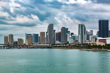 Fototapeta premium The modern Downtown Miami skyline rises dramatically above the turquoise waters of Biscayne Bay on a cloudy day.