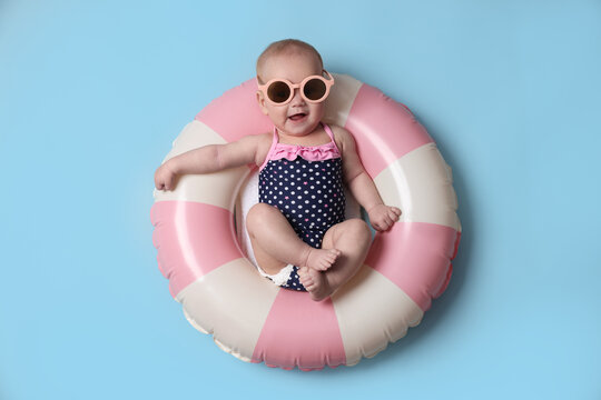Cute little baby with sunglasses on inflatable ring against light blue background, top view