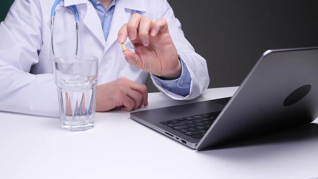 Doctor in a white coat showing a pill and having a glass of water on a desk with a laptop, representing telehealth, remote healthcare, and digital medical advice