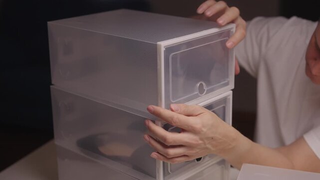 Close-up of man stacking clear plastic storage boxes filled with shoes, demonstrating effective organization and tidying solutions for footwear in home environment. Shooting in slow motion.