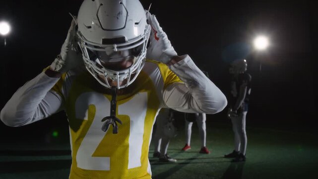 Medium portrait of young Caucasian male athlete, wearing yellow sports team jersey with number 21, putting on gridiron football with face mask, fastening while looking at camera with determination