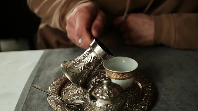 Man pouring traditional Bosnian coffee from a metal pot into a small cup on an ornate tray. Authentic coffee ceremony, slow preparation and cultural hospitality moment indoors. Horizontal 4k footage