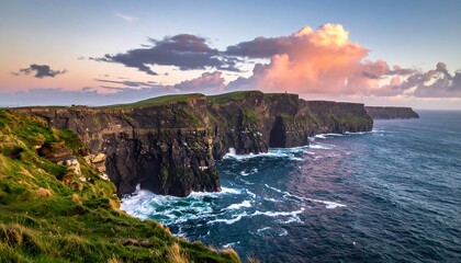 Jagged, green-topped cliffs meet a wavy ocean under a colorful sunset sky