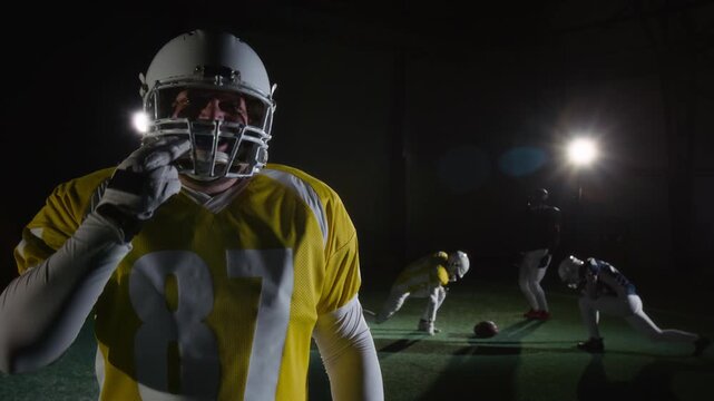 Medium portrait of young Caucasian male American football quarterback in team uniform putting in mouthguard, beating on helmet while challenging rivals to game with aggressive stare