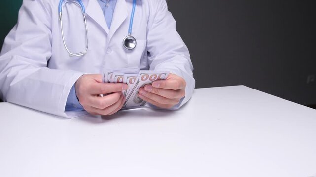 Doctor's hands in a white coat with a stethoscope around their neck are counting united states dollar banknotes on a plain white desk, symbolizing healthcare costs, corruption, and illicit payments - Powered by Adobe