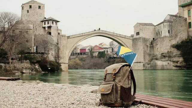 Backpack with the flag of Bosnia and Herzegovina placed by the river near the historic Stari Most bridge in Mostar. Travel lifestyle scene combining national identity, culture and iconic landscape