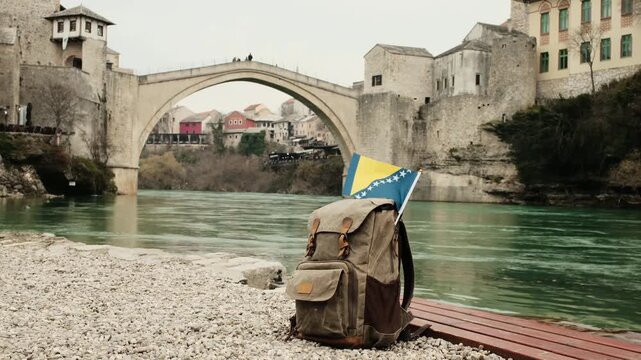 Backpack with the flag of Bosnia and Herzegovina placed by the river near the historic Stari Most bridge in Mostar. Travel lifestyle scene combining national identity, culture and iconic landscape