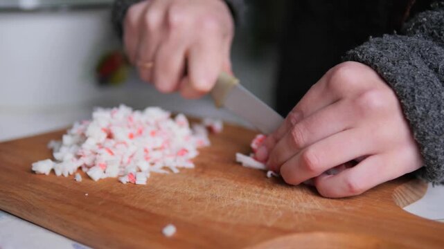 Hands Dicing Imitation Crab Sticks on Wooden Cutting Board for Salad Preparation