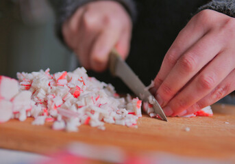 Obraz premium Close-up Action of Dicing Surimi Imitation Crab Sticks on a Wooden Board for Seafood Recipe
