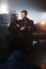Elegant gothic couple portrait featuring femme fatale in corseted black godet dress and man in formal black suit in dance-inspired embrace within luxurious dark interior. © Ulia Koltyrina