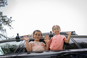 Little boy and girl waving and smiling from the car roof. High quality photo