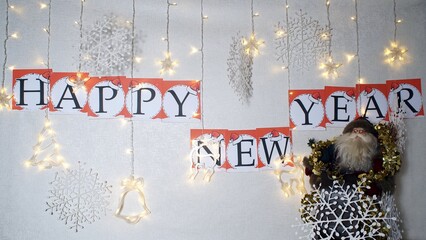 A garland is glowing ,decorative snowflakes,Santa Claus and a phrase happy new year made of decorative letters on the wall.