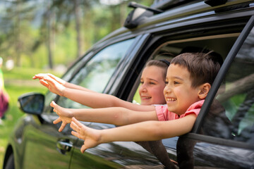 Two happy siblings looking out of car window enjoying summer breeze. High quality photo