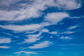 Soft clouds weave intricate patterns against a bright blue backdrop, creating serene beauty