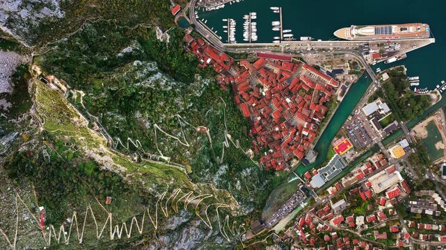 Aerial drone view of the famous zig zag hiking path leading to the fortress, next to the red roofs of Kotor Old Town and the marina