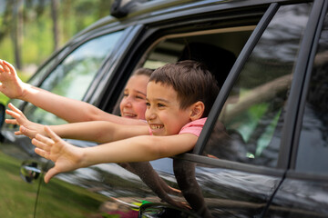 Excited kids waving from moving car window on family forest vacation. High quality photo