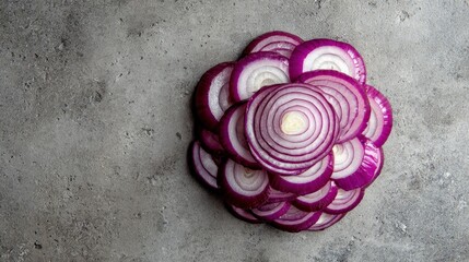 Overhead shot of a pile of sliced red onions arranged on a textured, grey, stone surface. The vibrant purple and white contrast