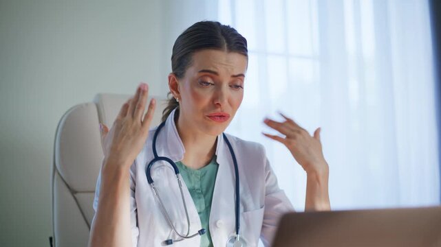 Healthcare provider video calling laptop gesturing hands at clinic table closeup