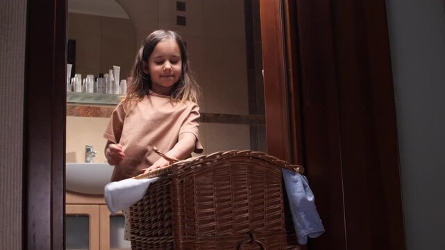 little girl joyfully manages laundry process, girl efficiently organizes clothes into laundry basket, Content girl finishes organizing clothing and places it into laundry basket with satisfaction