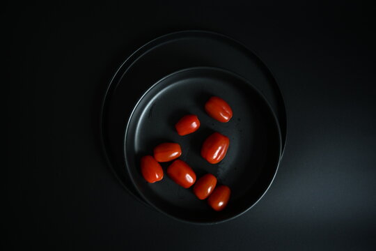 Creative food art: red plum tomatoes arranged in the shape of the number 1 on a black plate. Minimalist top view on dark background.