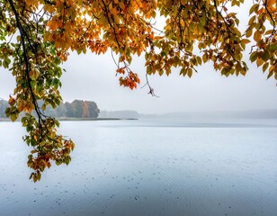 Lake view framed by autumn leaves in varied hues, mist hangs over the water,creating a peaceful, tranquil scene