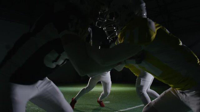 Medium full shot of American football players grappling in pairs on scrimmage line during training session at gridiron stadium, pushing against each other to develop blocking technique