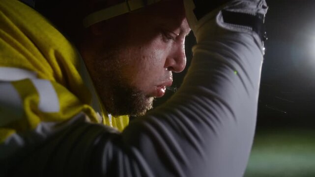 Side close-up of face of sweaty young Caucasian American football player removing helmet, spitting out mouthguard then drinking water from bottle during break in game or training session