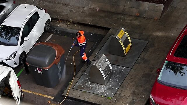 A municipal utility worker washing a garbage container with water. Spain, Barcelona 25.10.2025