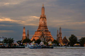 Fototapeta premium Majestic Wat Arun illuminated at dusk with the Chao Phraya River in the foreground in Bangkok