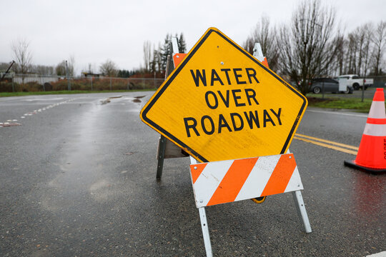 A road is closed due to flood water over the street. A large sign blocks traffic from moving forward.
