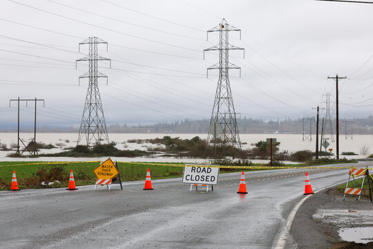 Road closed signs and caution tape warn drivers of flood water over the street preventing traffic from entering.
