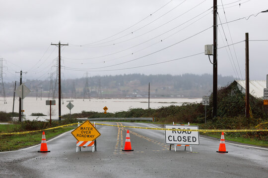 Road closed signs and caution tape warn drivers of flood water over the street preventing traffic from entering.