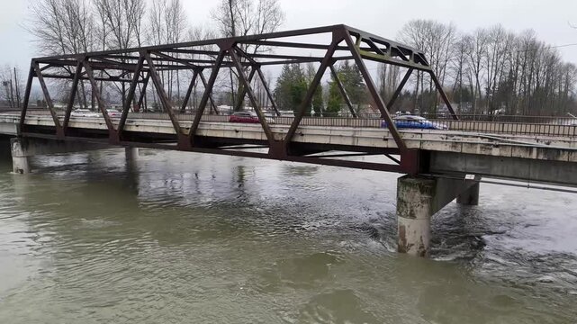 The Snohomish river in Washington state is at elevated levels due to flood water. Cars and vehicles drive over the river on a bridge. 