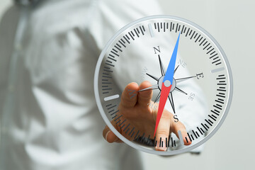 Fototapeta premium Close up of a hand holding a compass. The compass points towards the north. Navigation, direction, exploration, guidance, travel concept.