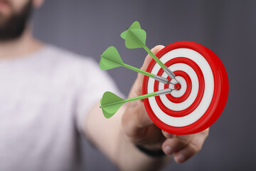 Close-up of a hand holding a dartboard with darts successfully hitting the bullseye. Concept of...