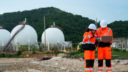 Petrochemical engineers in PPE conduct a site survey near LNG storage spheres. They use a laptop for data analysis and a radio for comms at the coastal refinery terminal.