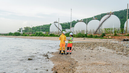 Environmental scientists in PPE conduct water testing near an LNG terminal. They use a portable analyzer and laptop to monitor pollution levels at the coastal refinery.
