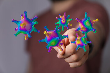 Abstract image of a hand holding a group of colorful, stylized coronavirus models, representing concepts like