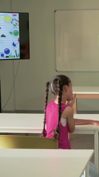 Vertical video: Turning student in pink top watching monitor in class after adult appears listening