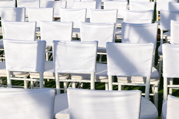 Outdoor rows of white Chiavari chairs with clean back covers on green lawn, sunlit and empty. Blank fabric ready for branding or text, ideal seating mockup for conference, wedding or event