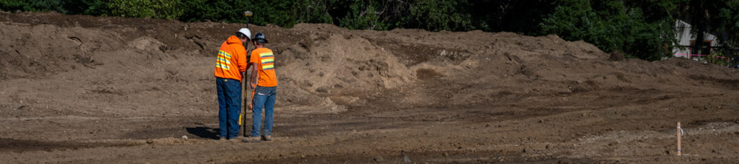 Two workmen using surveying equipment to mark new road location, new residential housing development construction site, sunny fall 
