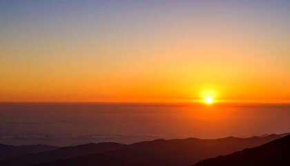 A vibrant sunrise over silhouetted mountain ridges, with a gradient sky of blues and oranges