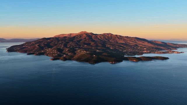 Aerial drone view of Corfu island near Ksamil, Albania showing rugged landscapes, green vegetation, and the island's coastline bathed in soft sunrise light
